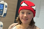 A young person wearing a red Spiderman beanie hat, in a hospital ward next a monitoring machine.